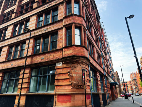 Historic red brick commercial building on a corner in Manchester, UK with ornate stonework, tall windows, Lena street lamps and urban sidewalk perspective