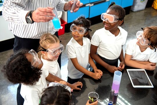 Children in a science class observing a teacher with a blue liquid.