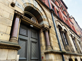 Obraz premium Historic Victorian architecture in Manchester, UK with arched stone facade, ornate granite columns and heavy wooden entrance door on a redbrick civic building