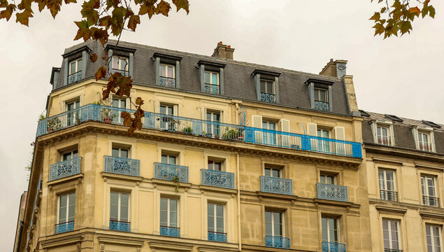 Haussmann building facade in Paris featuring blue balconies and autumn leaves on an overcast day