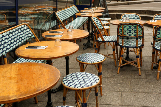Empty outdoor tables and chairs at a traditional Parisian cafe terrace, ready for customers on a classic cobbled street