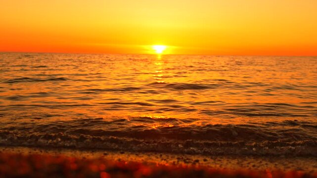 Vivid sunset illumination captures rhythmic coastal waves rolling toward a gravel shore during twilight. Wide angle fixed tripod shot.