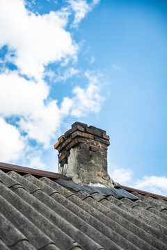 Aged brick chimney rising from a weathered corrugated roof under a bright blue sky in Ukraine. 