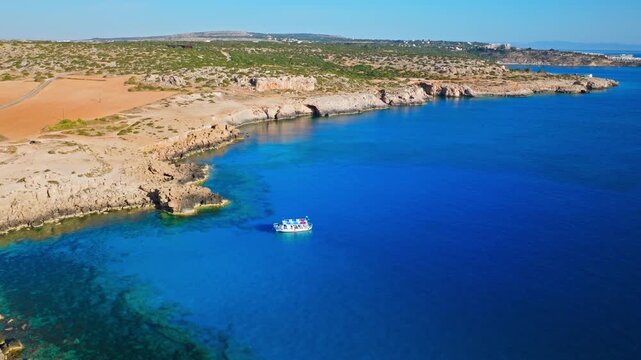Drone view of the coastline in Cavo Greco National Park, Cyprus. A curved bay, deep blue water and dry rocky land create a striking Mediterranean scene.