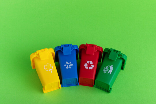 Four colorful recycling bins with waste icons on a green background, symbolizing sorting and environmental awareness.