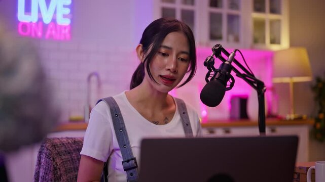 Smiling young asian woman recording podcast from her home studio.Joyful woman recording live podcast.Vlogger live streaming podcast review on social media,Asian woman use microphones wear headphones