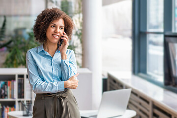 Fototapeta na wymiar Smiling black businesswoman talking on smartphone standing