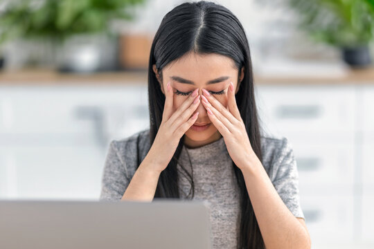 Tired Asian woman rubbing eyes at laptop