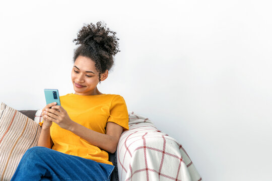 Happy Black woman using smartphone on sofa