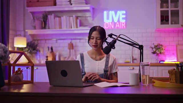 Smiling young asian woman recording podcast from her home studio.Joyful woman recording live podcast.Vlogger live streaming podcast review on social media,Asian woman use microphones wear headphones