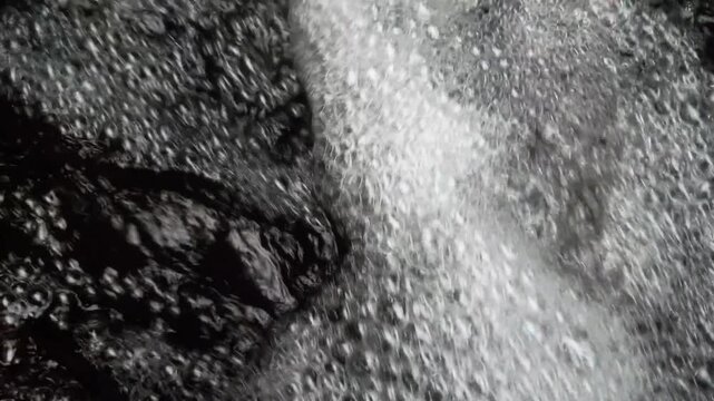 Abstract Black and White Texture Featuring Turbulent Rushing Water Flowing Over Dark Jagged Rocks in a Natural River Setting