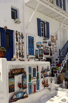 Traditional Mykonos souvenir shop with whitewashed walls, blue shutters, colorful doors, and handcrafted nautical decorations.