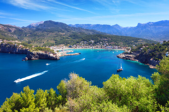 Picturesque views of rocky shore Port de Soller, bathed by azure waters of Mediterranean Sea. Lighthouse can be seen in distance,