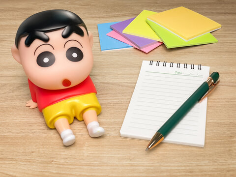 Thailand, Phuket &ndash; July 18, 2026: A Crayon Shin-chan anime character phone holder sits on a desk next to a notepad, pen, and colorful sticky notes. Suitable for study, office.