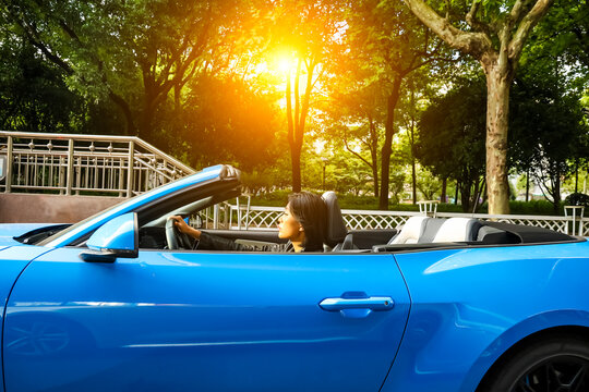An Asian woman drives a blue convertible sports car down the street.