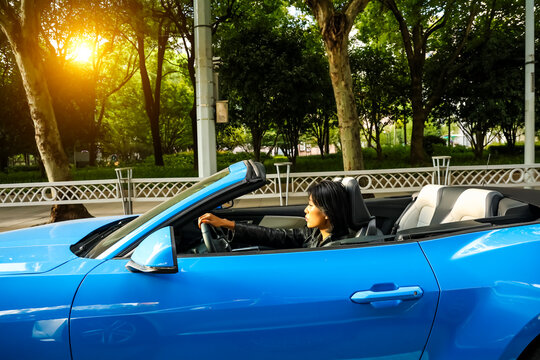 An Asian woman drives a blue convertible sports car down the street.