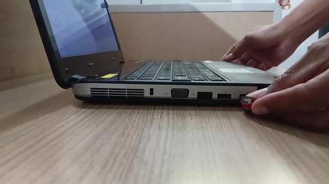 Close-up footage of a hand inserting a USB flash drive into a laptop. Concept of data transfer, technology, digital storage, computer accessories, office work, and everyday laptop use.