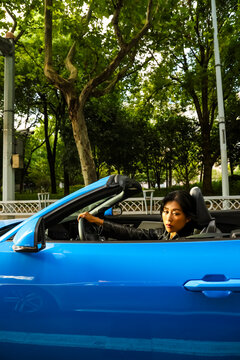 An Asian woman drives a blue convertible sports car down the street.