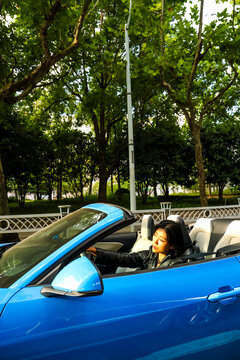 An Asian woman drives a blue convertible sports car down the street.