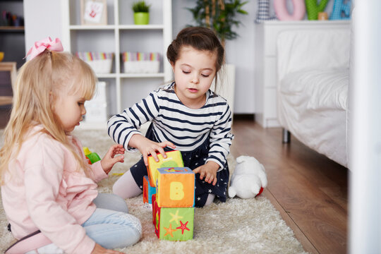 Two little girls playing with toy blocks on carpet at home