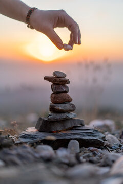 Close-up of man's hand placing stone on cairn at sunset
