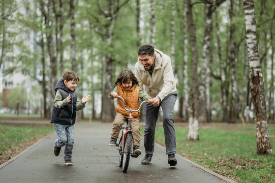 Boy cheering brother learning to ride bicycle with father at park
