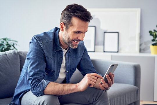 Smiling man sitting on sofa using cell phone