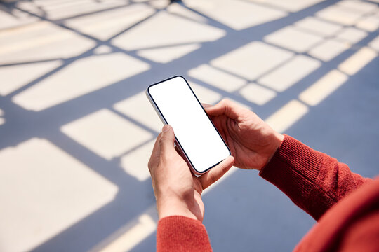Hands holding a blank smartphone mockup outdoors in sunlight
