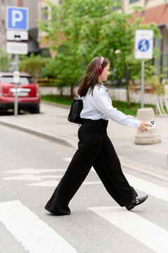 Woman in blue shirt walks on crosswalk listening to music