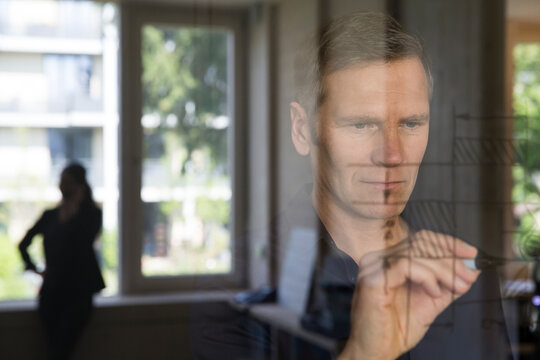 Portrait of business man drawing sketch on glass pane