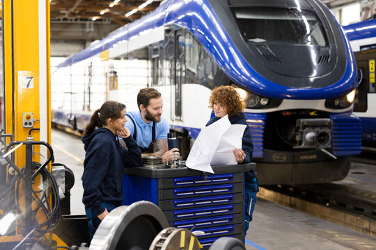 Trainees discussing with engineer over blueprint at factory