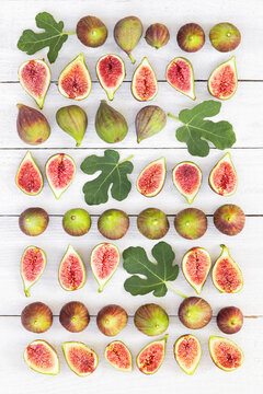 Fresh whole and halved figs form a pattern on a white wooden table