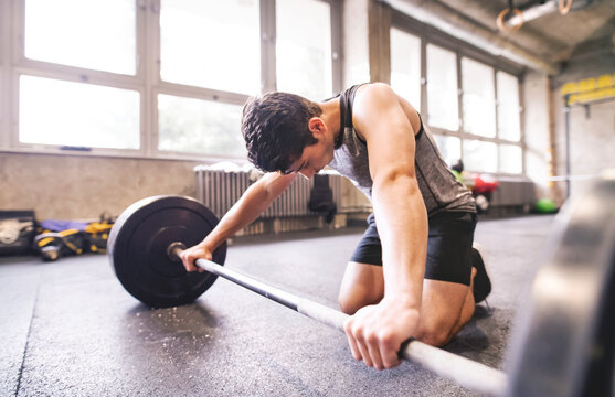 Young athlete exercising with barbell in gym