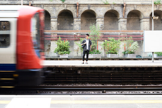 Young man listening music with headphones, standing on station