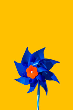 A blue plastic pinwheel stands against a yellow background