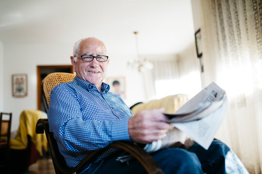 Portrait of smiling senior man with newspaper at home