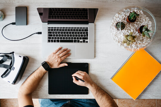 Man working with graphics tablet and laptop at home office, top view