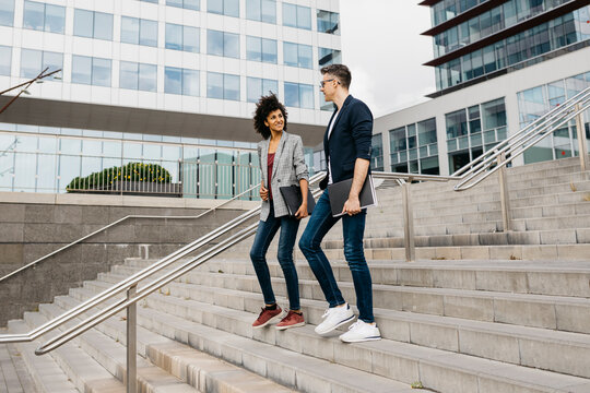 Two colleagues walking and talking on stairs outside office building in the city