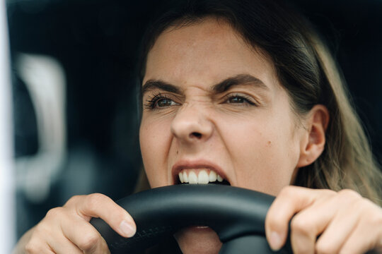 Close-up of angry woman biting steering wheel while while sitting in car