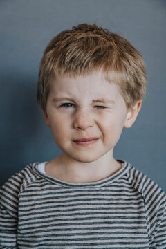 Playful boy winking against gray background