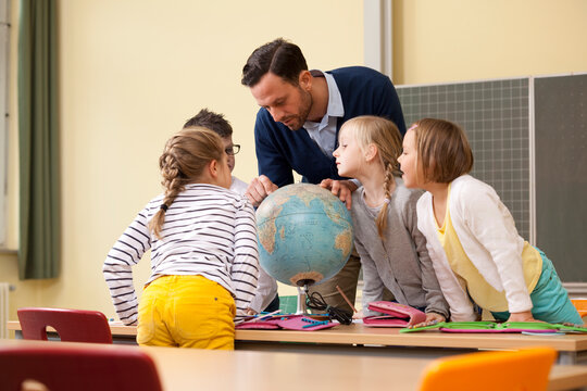 Teacher and pupils looking at globe in classroom