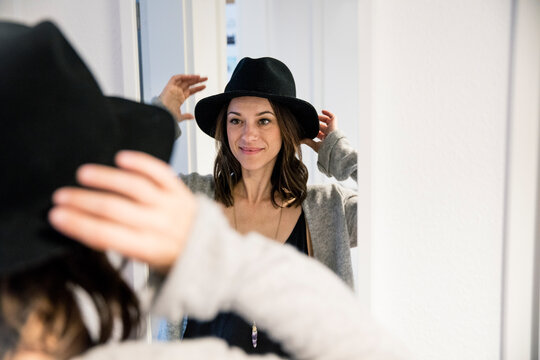Mature woman standing in front of mirror , putting on a hat