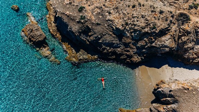 Woman floats in turquoise sea near rocky cove during summer