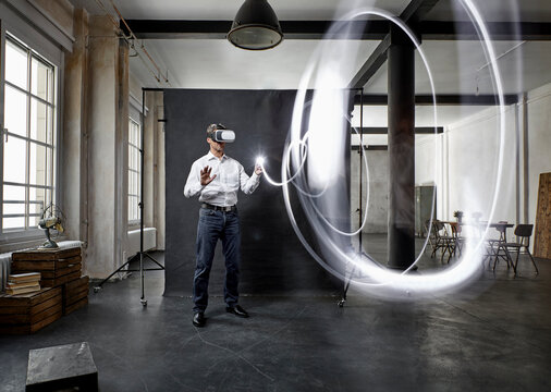Mature man with vr glasses light painting in front of black backdrop in loft