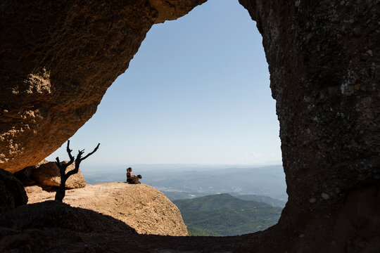 Woman sits with dog on a mountain ledge in Montserrat Spain