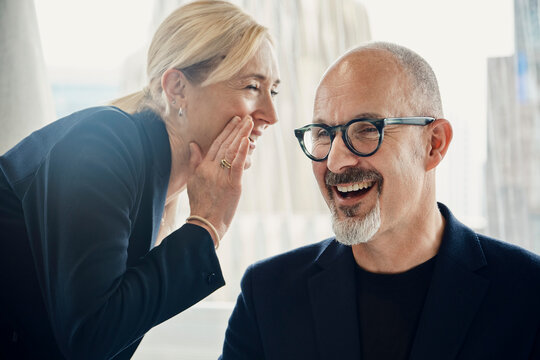 A businesswoman whispers a funny joke to a businessman in the office