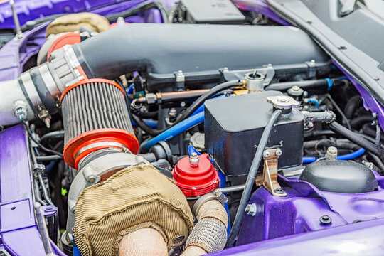 Close-up view of high-performance engine bay, featuring horizontally opposed boxer engine, air intake system, hoses, and wires, vibrant purple paint contrasting metallic components