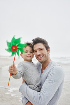 Father carrying son on the beach holding green pinwheel