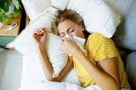 Ill woman wiping nose with tissue in bed at home