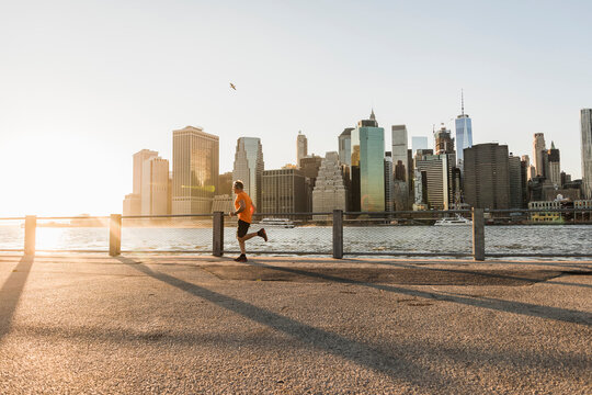USA, Brooklyn, man jogging in front of Manhattan skyline in the evening